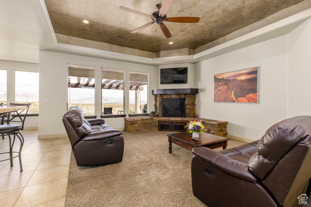 Living room with a tray ceiling, ceiling fan, light tile patterned floors, and a stone fireplace