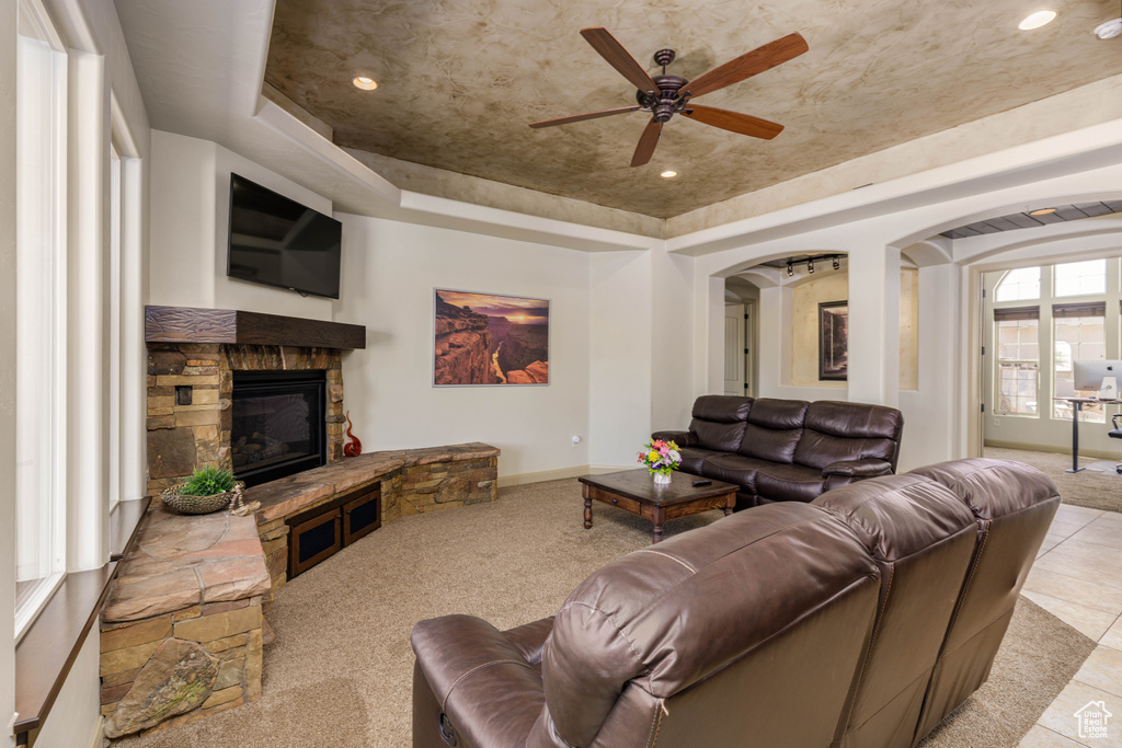 Living area with a raised ceiling, arched walkways, ceiling fan, a fireplace, and recessed lighting