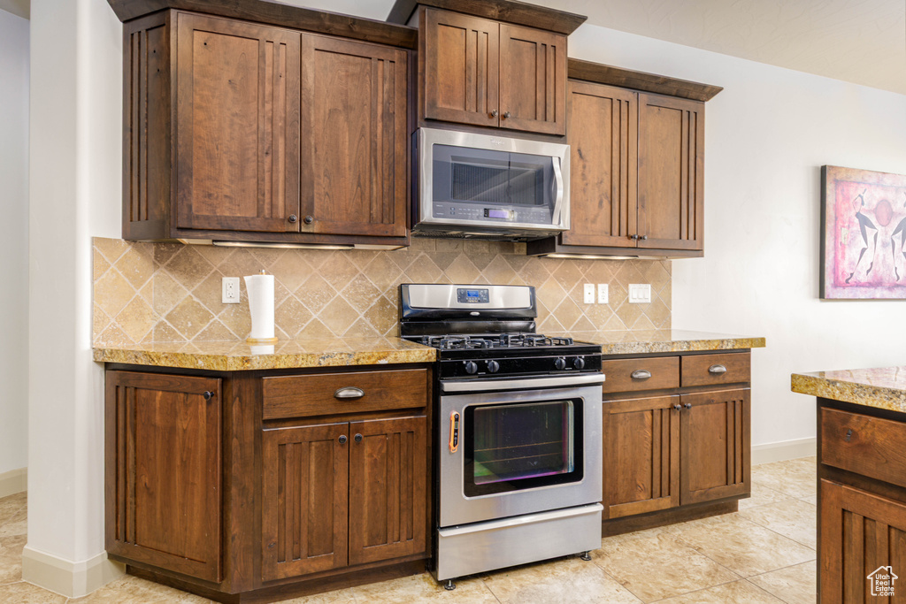 Kitchen featuring appliances with stainless steel finishes, decorative backsplash, light stone countertops, and light tile patterned floors