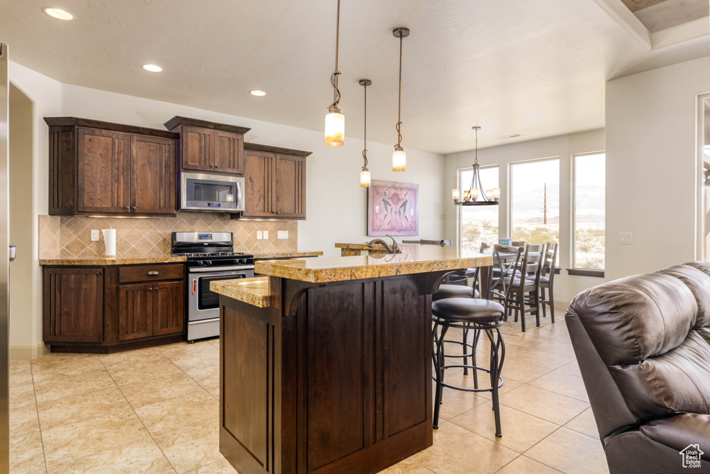 Kitchen with appliances with stainless steel finishes, open floor plan, a kitchen bar, tasteful backsplash, and a chandelier