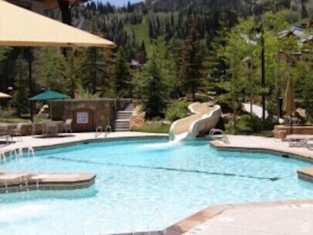 Community pool featuring a water slide, a view of trees, and stairway