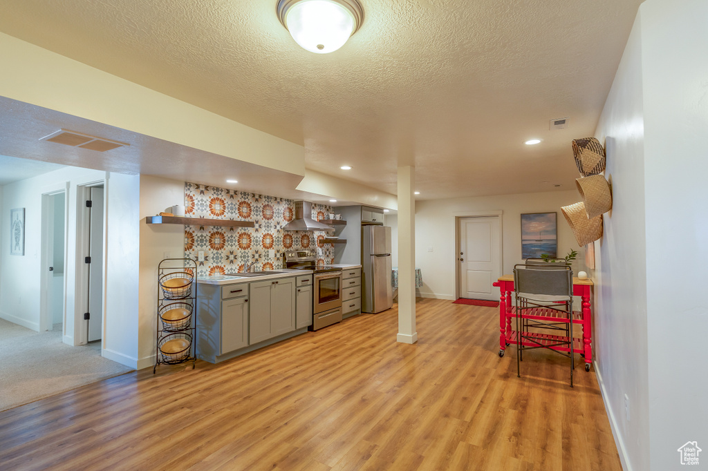 Kitchen featuring stainless steel appliances, wall chimney exhaust hood, open shelves, light wood-style flooring, and gray cabinets