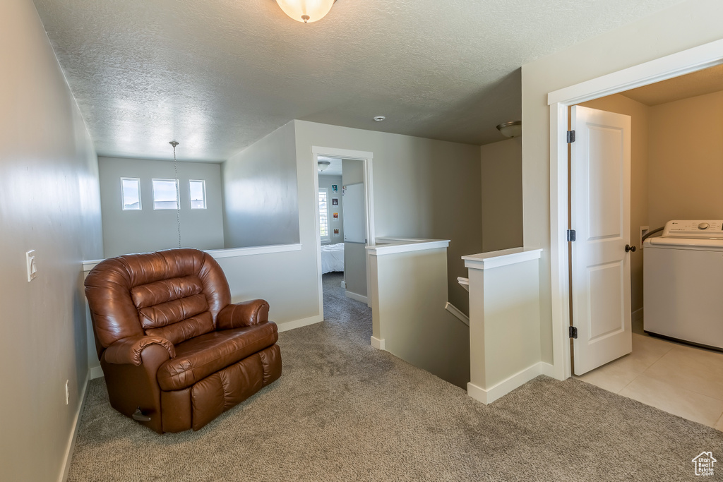 Living area with washer / clothes dryer, an upstairs landing, a textured ceiling, and light carpet
