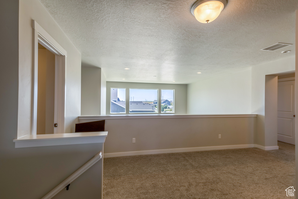 Carpeted empty room featuring a textured ceiling and baseboards