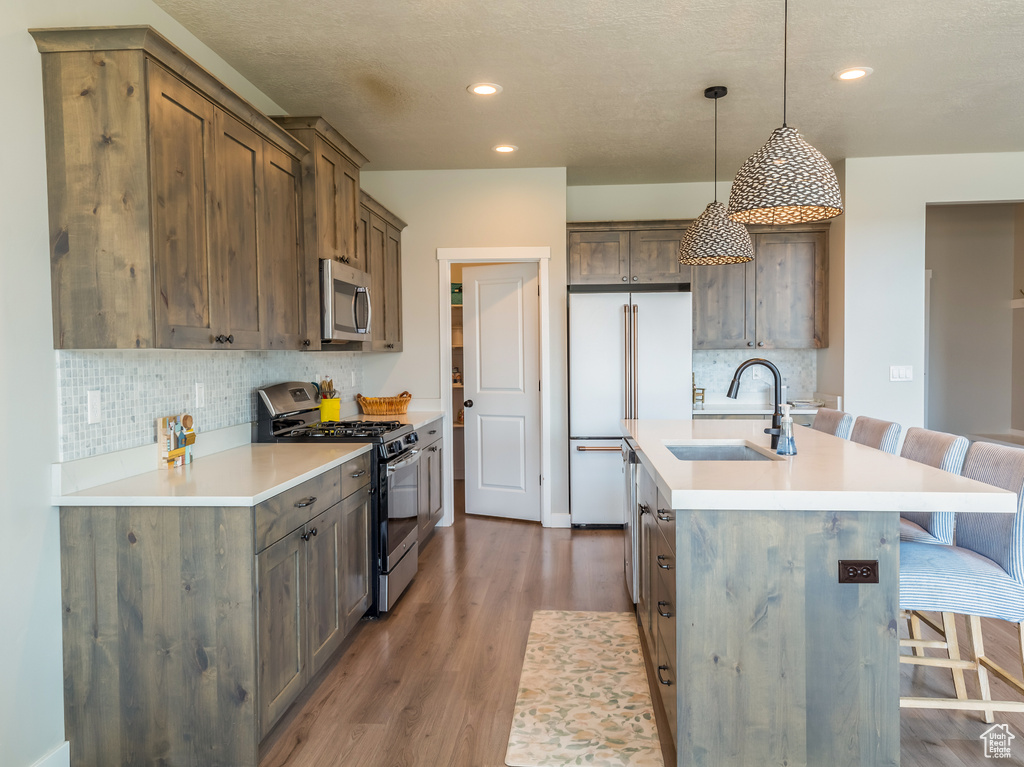 Kitchen featuring stainless steel appliances, a breakfast bar area, decorative backsplash, wood finished floors, and a kitchen island with sink