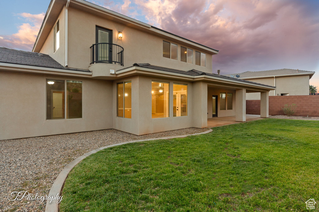 Back of house at dusk with a balcony, a patio area, and stucco siding