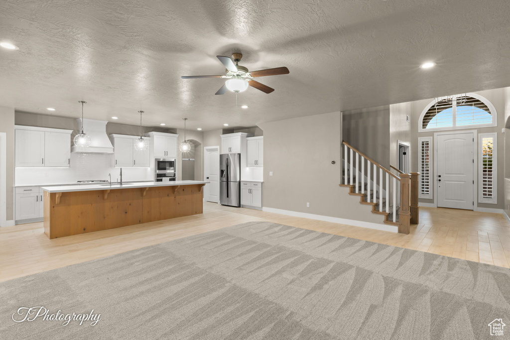 Kitchen with stainless steel appliances, open floor plan, light wood-style floors, a large island with sink, and a ceiling fan