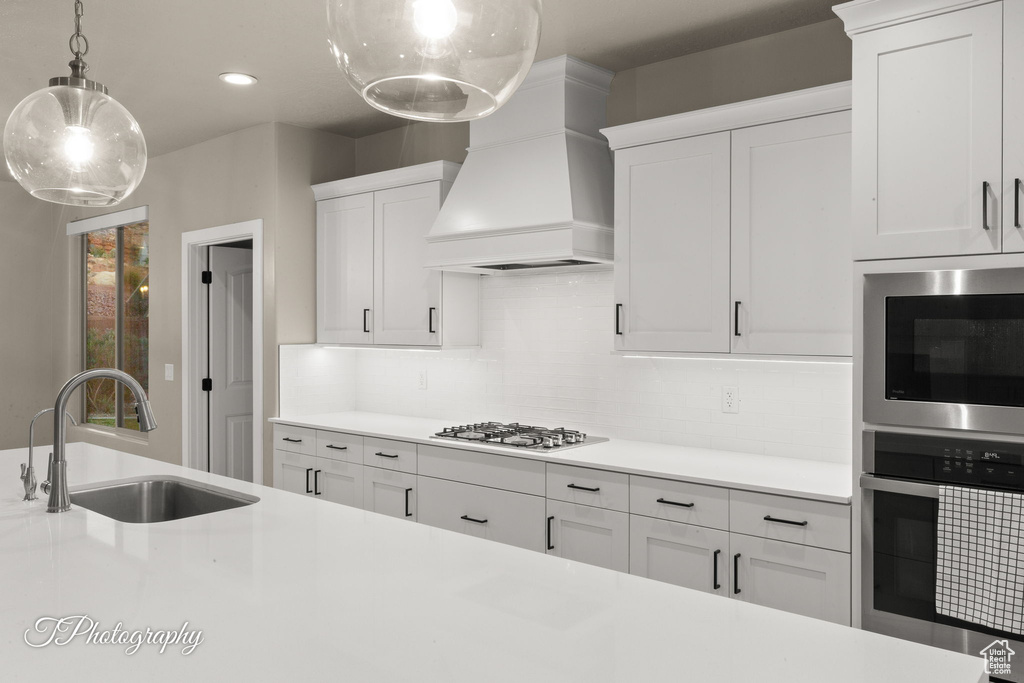 Kitchen with gas cooktop, light countertops, premium range hood, decorative backsplash, and stainless steel microwave