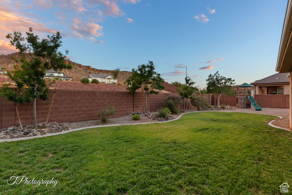 Yard at dusk featuring a playground and a fenced backyard
