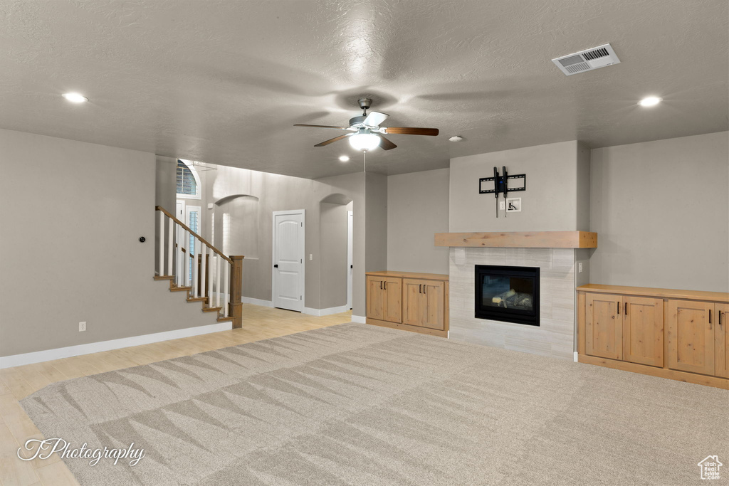 Unfurnished living room with arched walkways, a ceiling fan, a tile fireplace, recessed lighting, and stairs