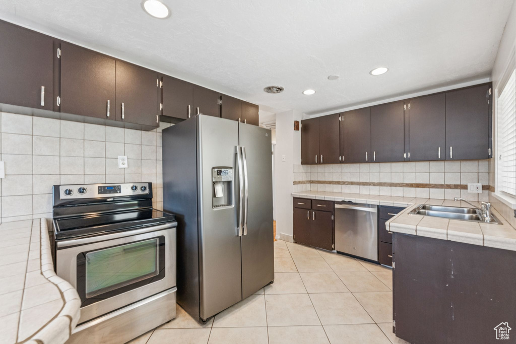 Kitchen with stainless steel appliances, dark brown cabinetry, tasteful backsplash, light tile patterned floors, and recessed lighting