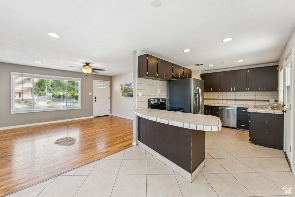 Kitchen with appliances with stainless steel finishes, tile countertops, a peninsula, decorative backsplash, and open floor plan