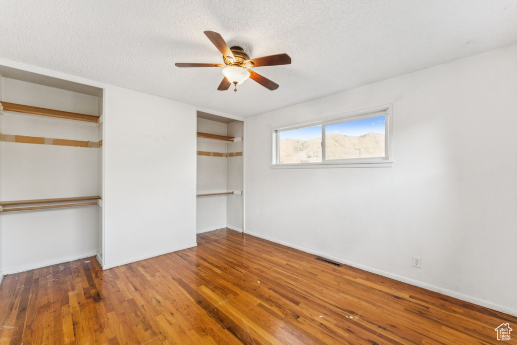 Unfurnished bedroom with a textured ceiling, wood finished floors, multiple closets, and a ceiling fan