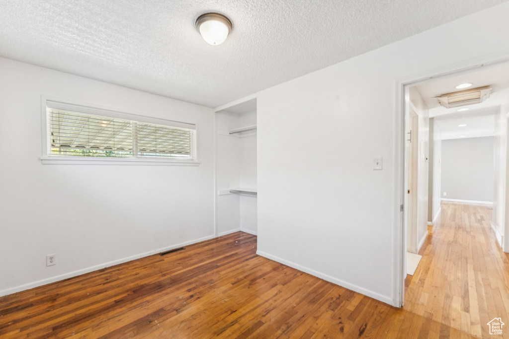 Unfurnished bedroom with hardwood / wood-style floors, a closet, a textured ceiling, and attic access