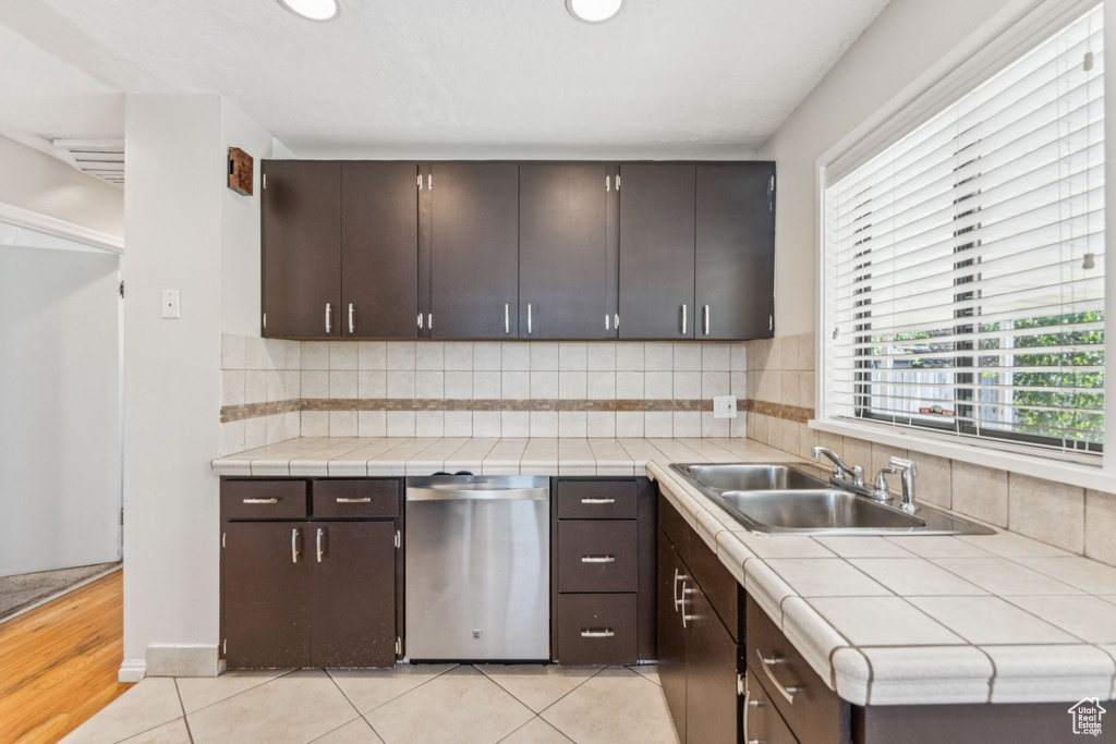 Kitchen with stainless steel dishwasher, backsplash, light tile patterned flooring, dark brown cabinetry, and recessed lighting