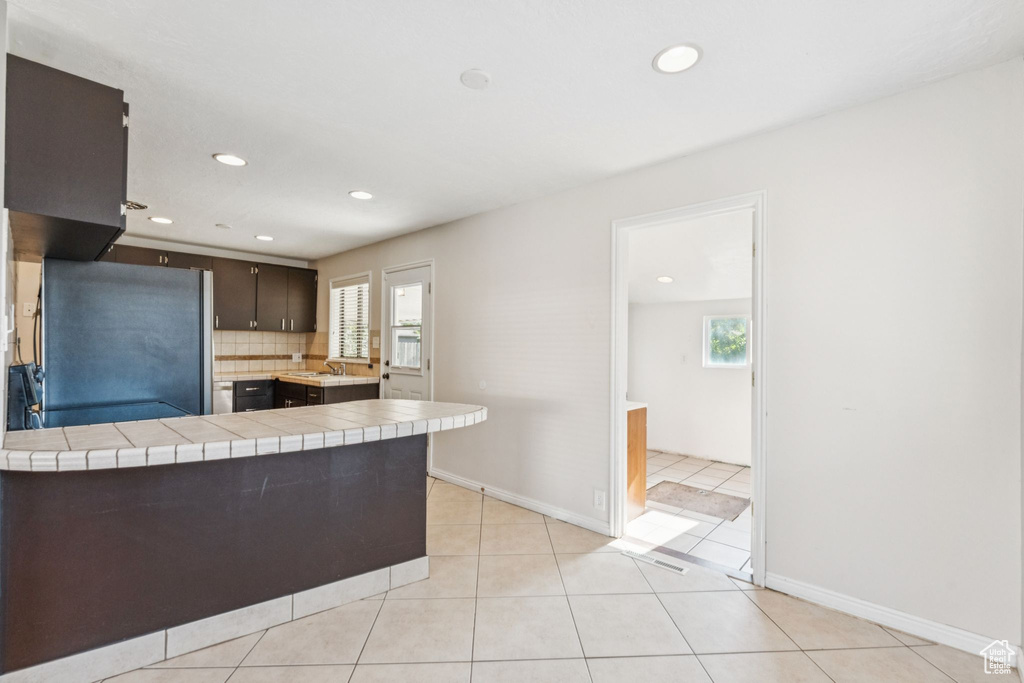 Kitchen featuring freestanding refrigerator, tile countertops, dark brown cabinets, a peninsula, and recessed lighting