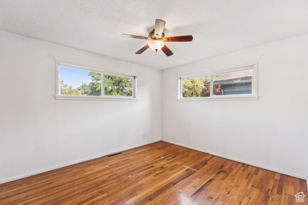 Empty room with wood finished floors, a ceiling fan, and a textured ceiling