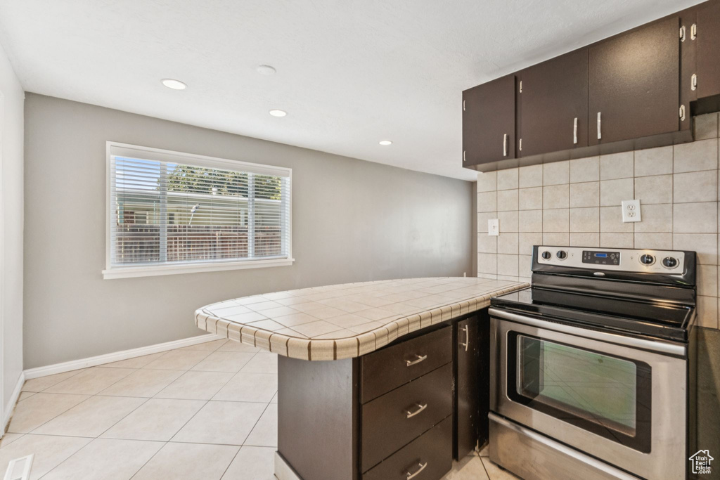 Kitchen featuring stainless steel range with electric stovetop, a peninsula, decorative backsplash, recessed lighting, and tile countertops