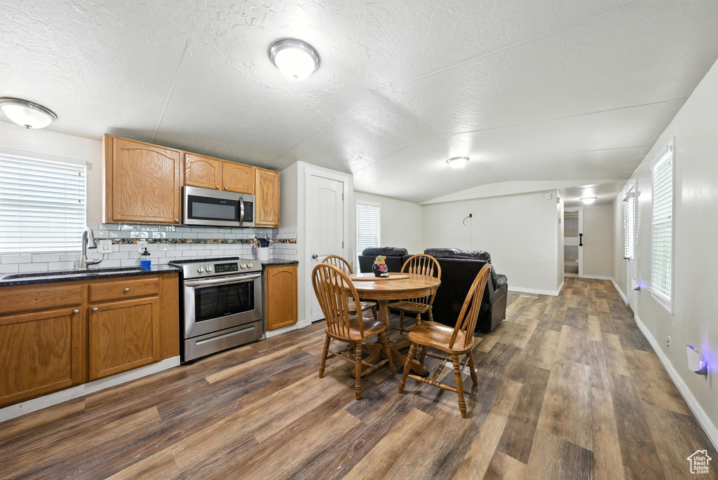 Kitchen with stainless steel appliances, dark countertops, dark wood-style flooring, vaulted ceiling, and decorative backsplash