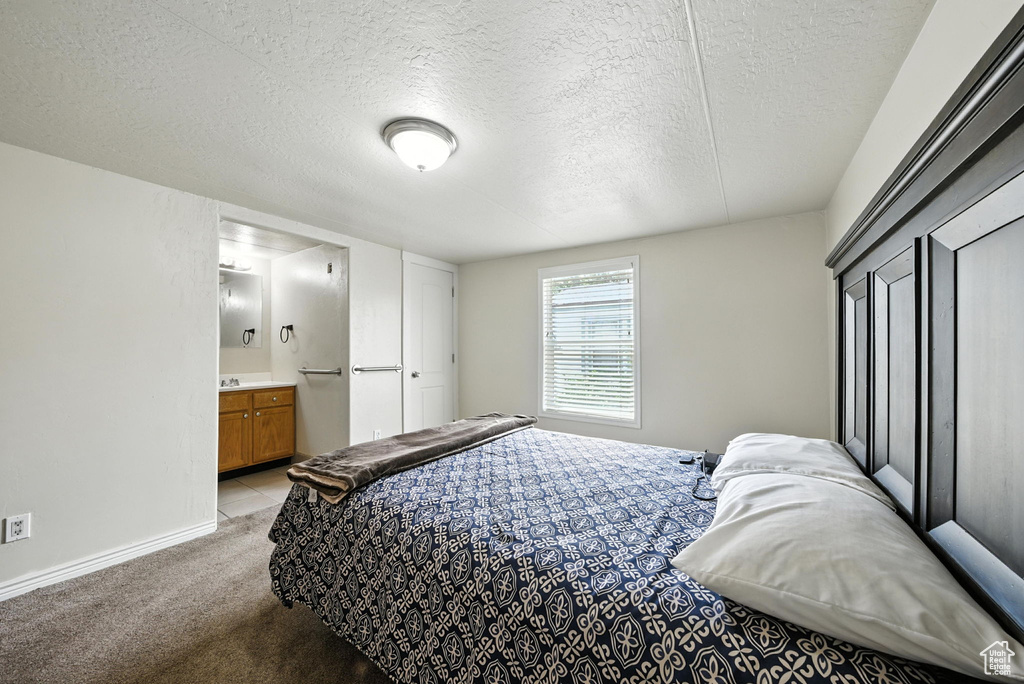 Bedroom with light carpet, a textured ceiling, and ensuite bath