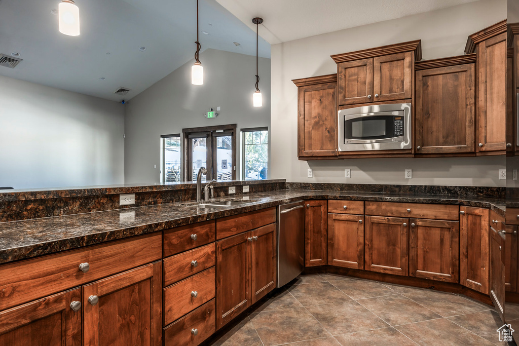 Kitchen featuring appliances with stainless steel finishes, high vaulted ceiling, dark stone countertops, hanging light fixtures, and dark tile patterned floors