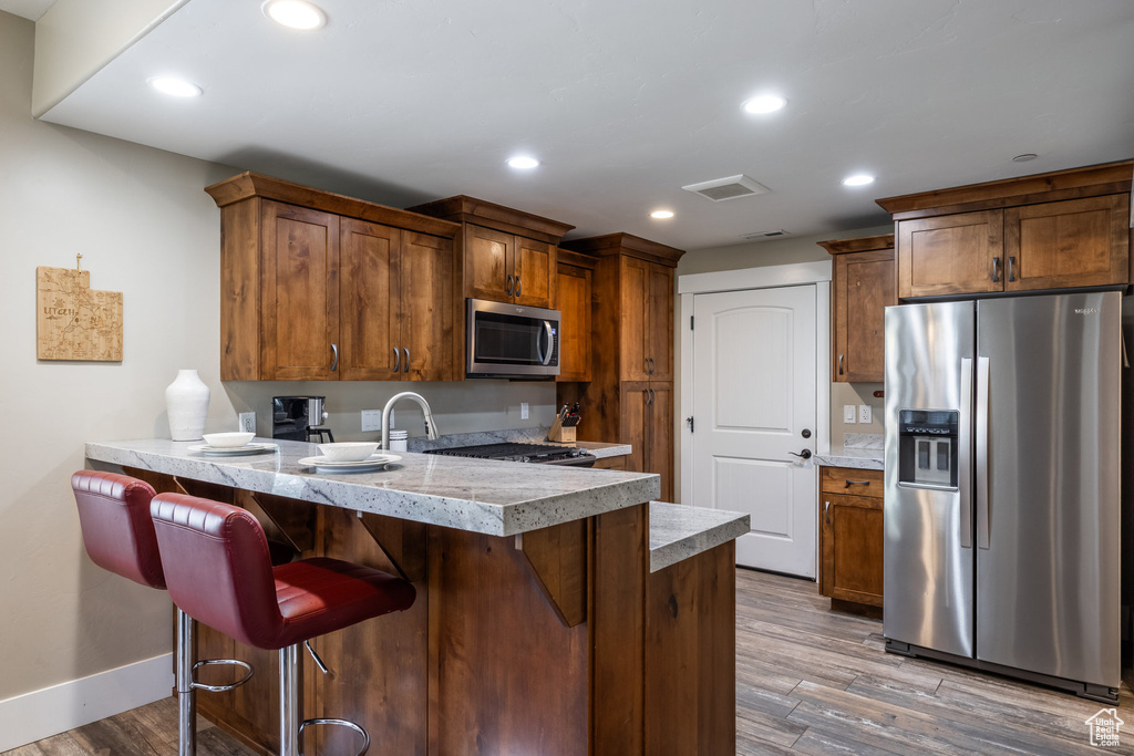 Kitchen with appliances with stainless steel finishes, a peninsula, wood finished floors, light countertops, and a kitchen breakfast bar