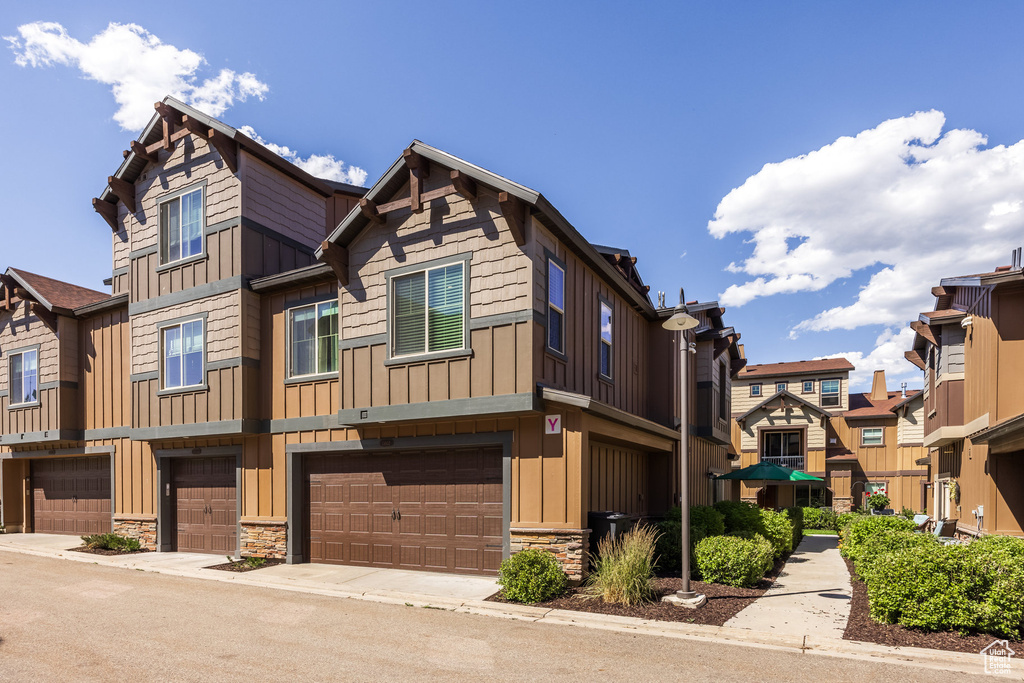 Townhome / multi-family property featuring board and batten siding, an attached garage, stone siding, and a residential view