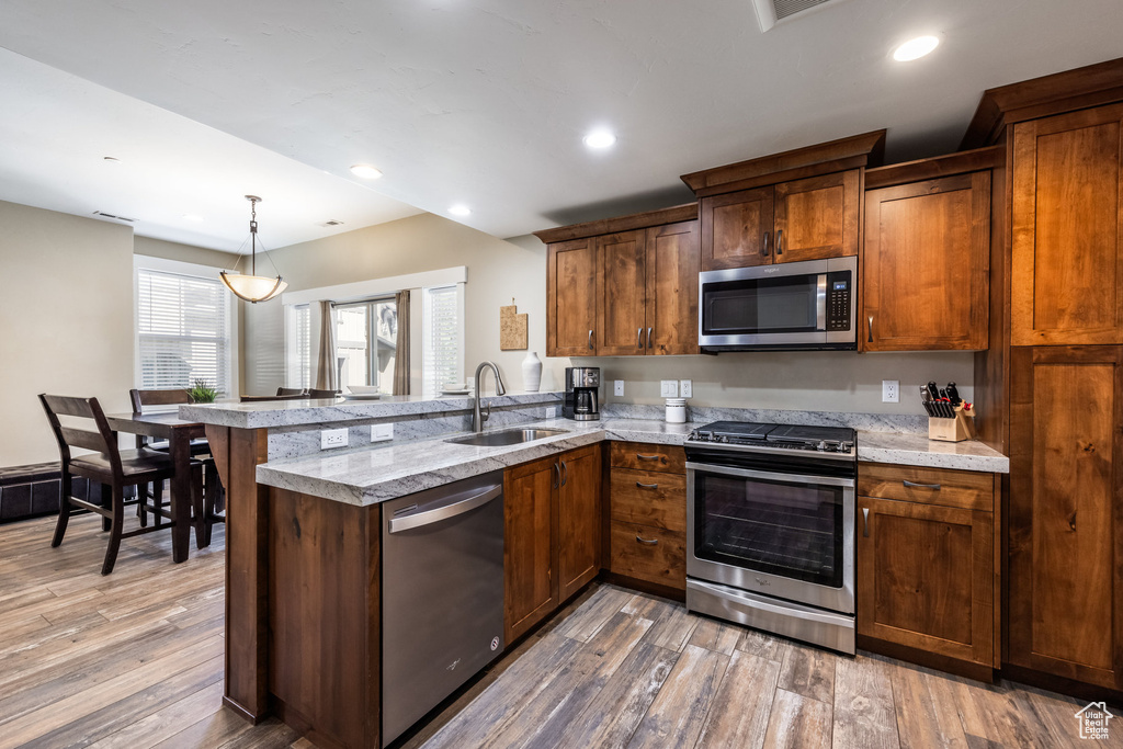 Kitchen with stainless steel appliances, a peninsula, light wood-style floors, recessed lighting, and decorative light fixtures