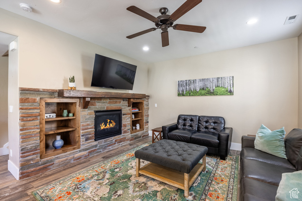 Living area with wood finished floors, ceiling fan, a stone fireplace, and recessed lighting