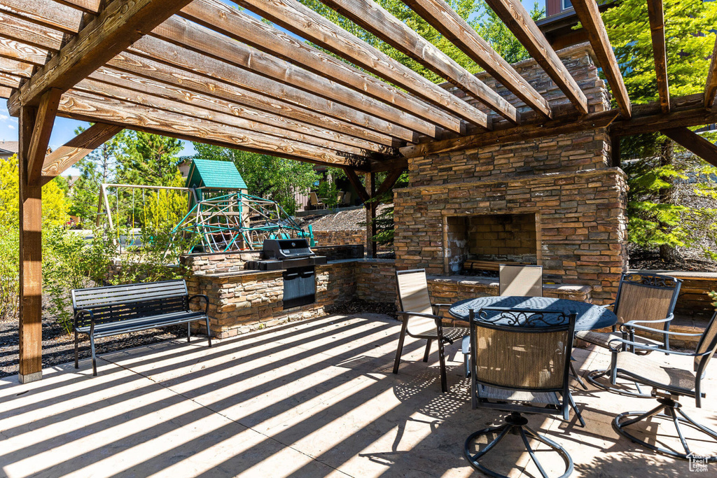View of patio featuring an outdoor stone fireplace, a pergola, a playground, and outdoor dining area
