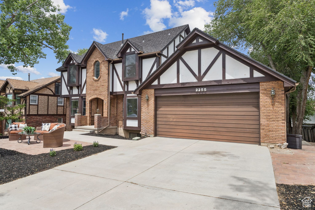 Tudor home with an attached garage, driveway, an outdoor living space, brick siding, and stucco siding