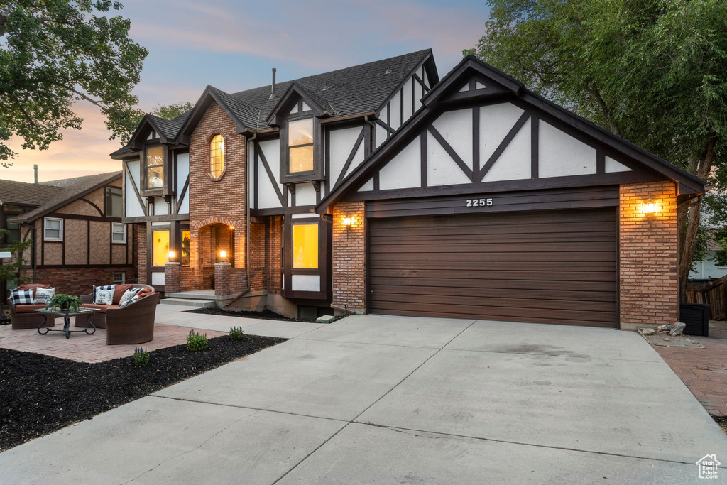 Tudor home featuring brick siding, an outdoor living space, a garage, concrete driveway, and stucco siding