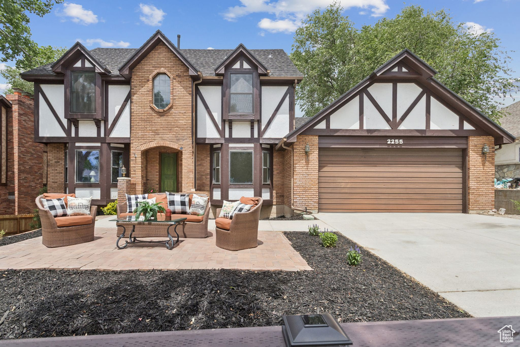 Tudor house with an outdoor hangout area, a garage, driveway, a shingled roof, and brick siding