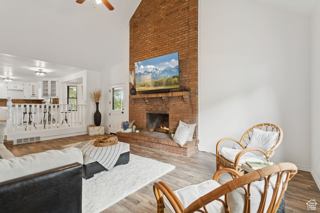 Living room featuring high vaulted ceiling, ceiling fan, a fireplace, and wood finished floors