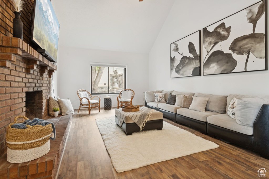 Living area with wood finished floors, high vaulted ceiling, and a brick fireplace