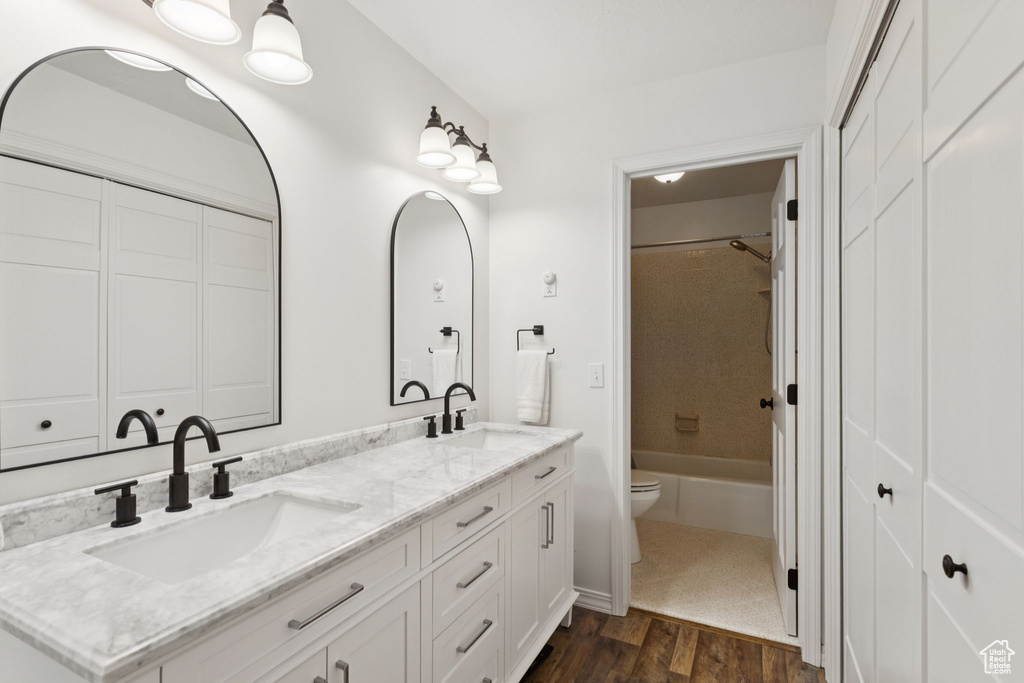 Full bathroom with wood finished floors, double vanity, and shower / washtub combination