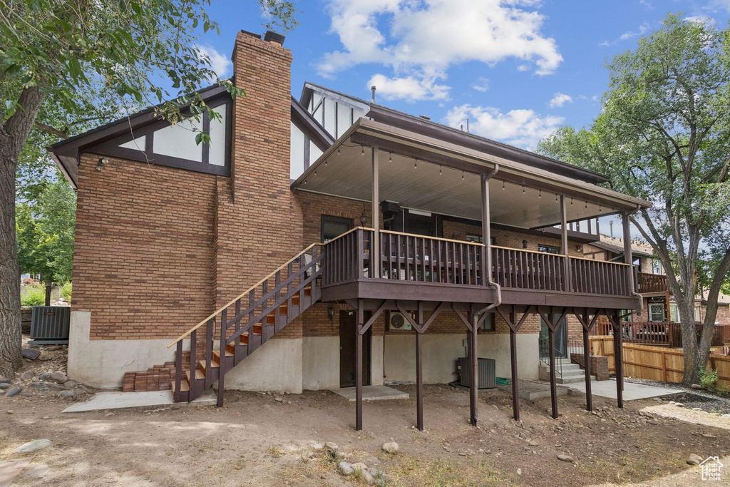 Back of house with a chimney, stairs, brick siding, and a wooden deck