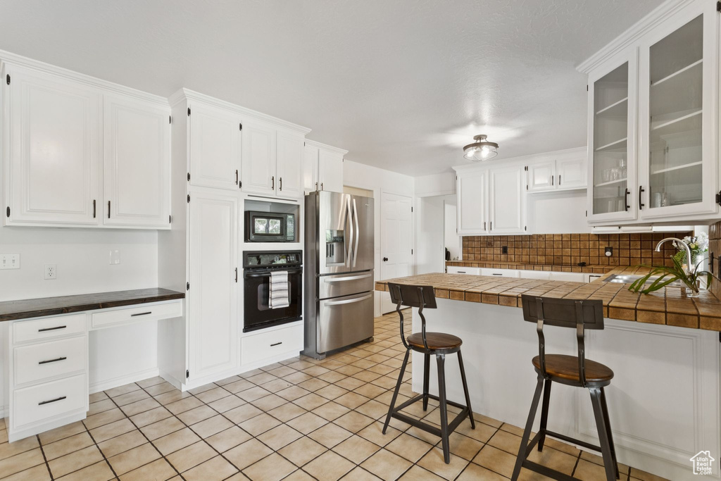Kitchen with oven, stainless steel fridge, built in microwave, a peninsula, and a kitchen bar