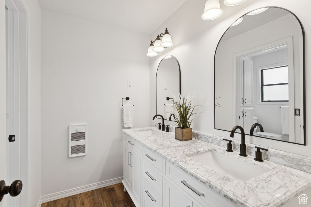 Bathroom with double vanity, heating unit, and wood finished floors