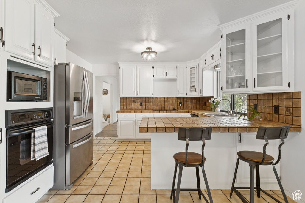 Kitchen with oven, stainless steel fridge, a peninsula, built in microwave, and backsplash