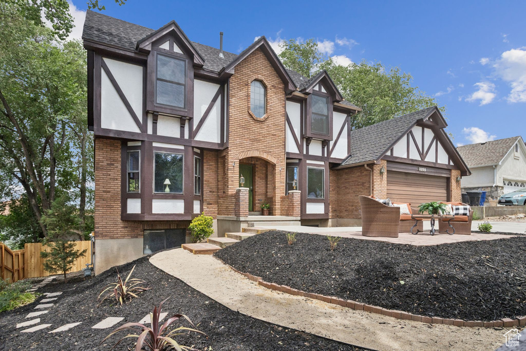 Tudor home with brick siding, an outdoor hangout area, an attached garage, roof with shingles, and stucco siding