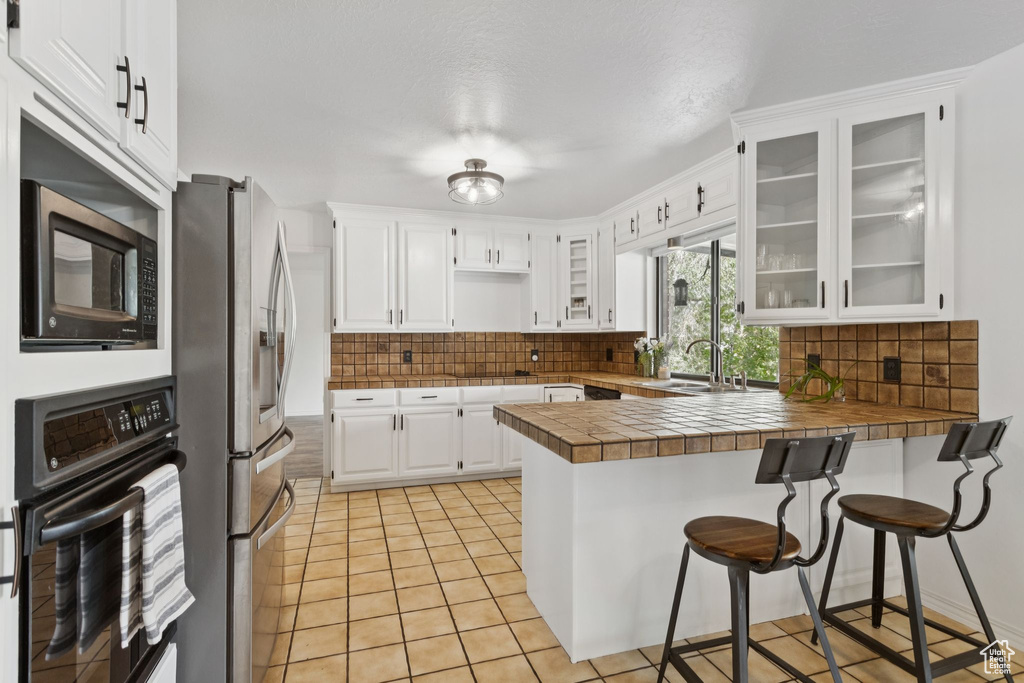 Kitchen with black appliances, a peninsula, decorative backsplash, and white cabinetry