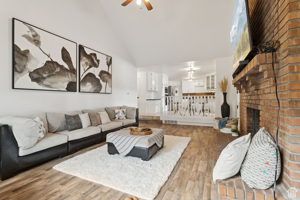 Living area with a ceiling fan, high vaulted ceiling, wood finished floors, and a fireplace