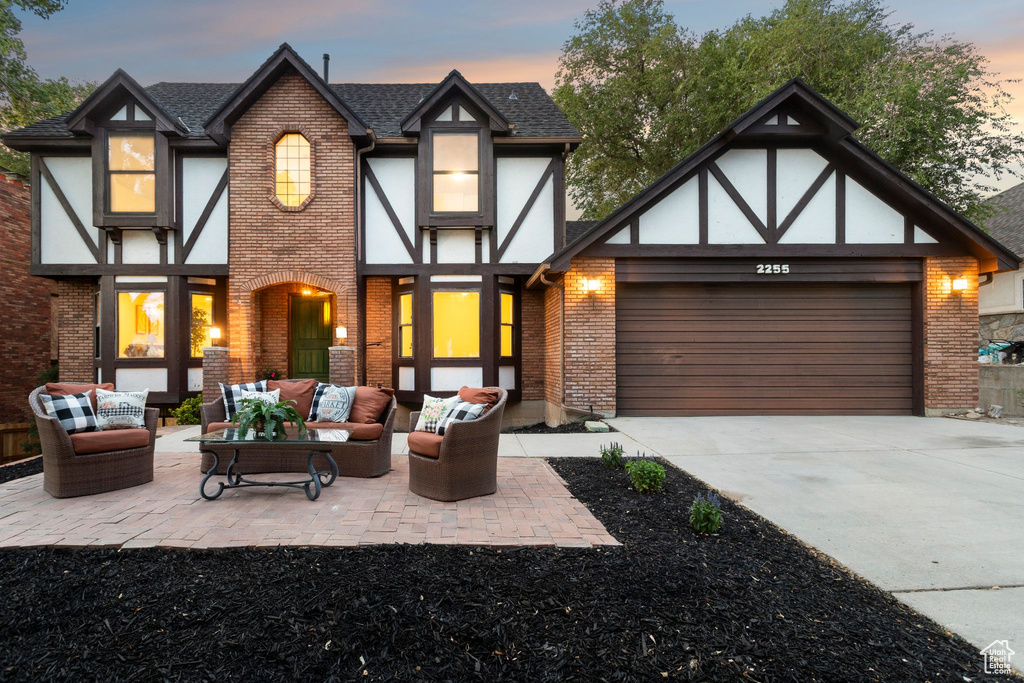 View of front facade featuring brick siding, an outdoor hangout area, concrete driveway, a garage, and roof with shingles
