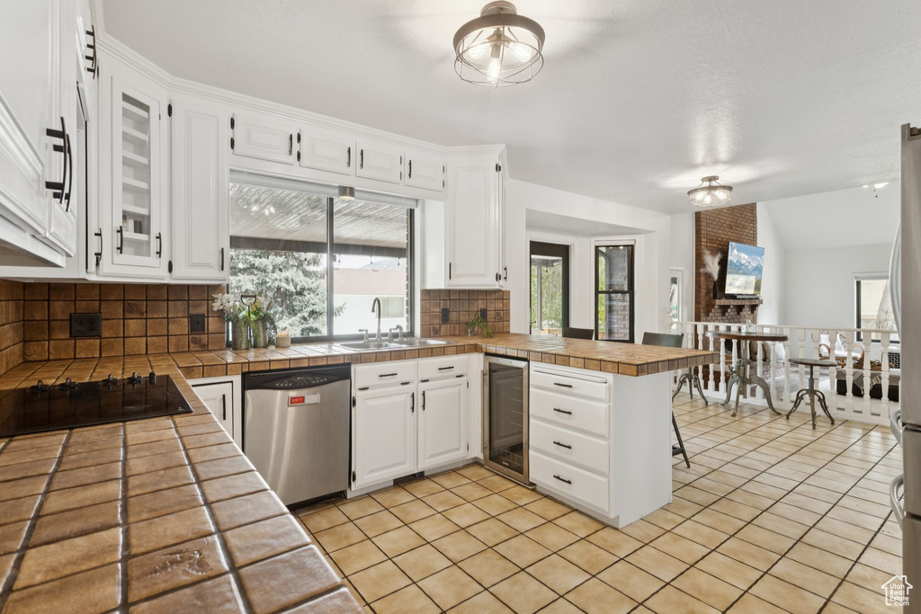 Kitchen with stainless steel dishwasher, wine cooler, a peninsula, backsplash, and black electric cooktop