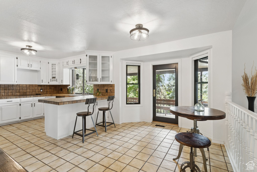 Kitchen featuring a breakfast bar, a peninsula, light tile patterned floors, and backsplash