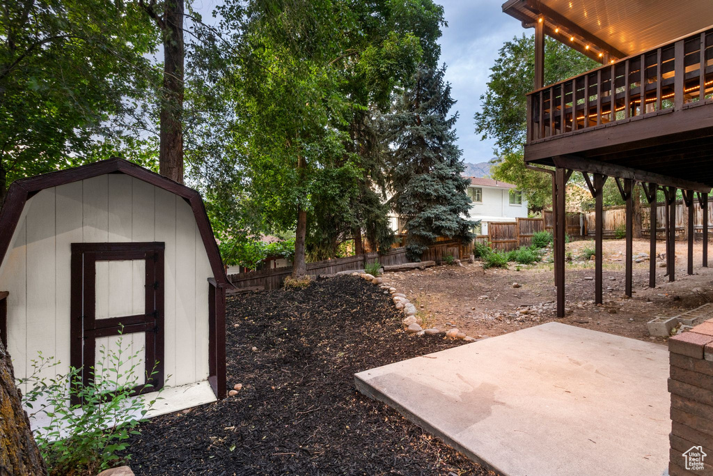 Fenced backyard featuring a patio, a storage unit, and a wooden deck