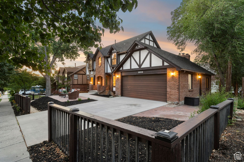 Tudor house featuring brick siding, an attached garage, driveway, and a chimney