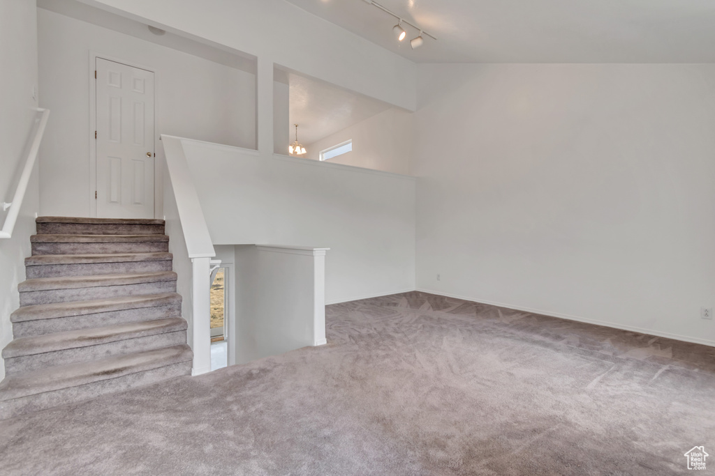 Unfurnished living room featuring carpet flooring, rail lighting, and stairs