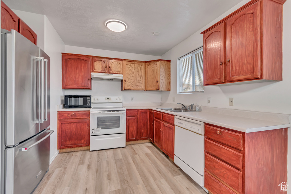 Kitchen featuring white appliances, light wood-type flooring, light countertops, and under cabinet range hood